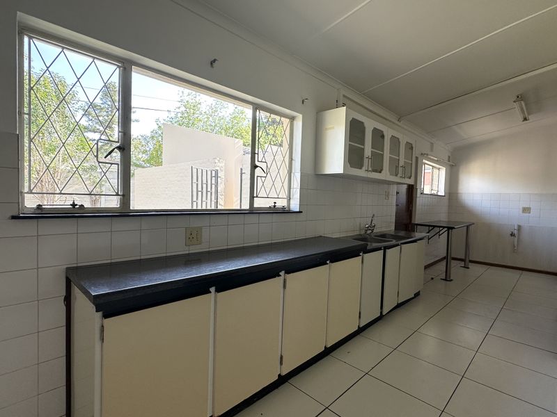 A functional, empty kitchen featuring tiled flooring, ample built-in cabinetry, laminate countertops, and a double basin sink with natural light from large windows.