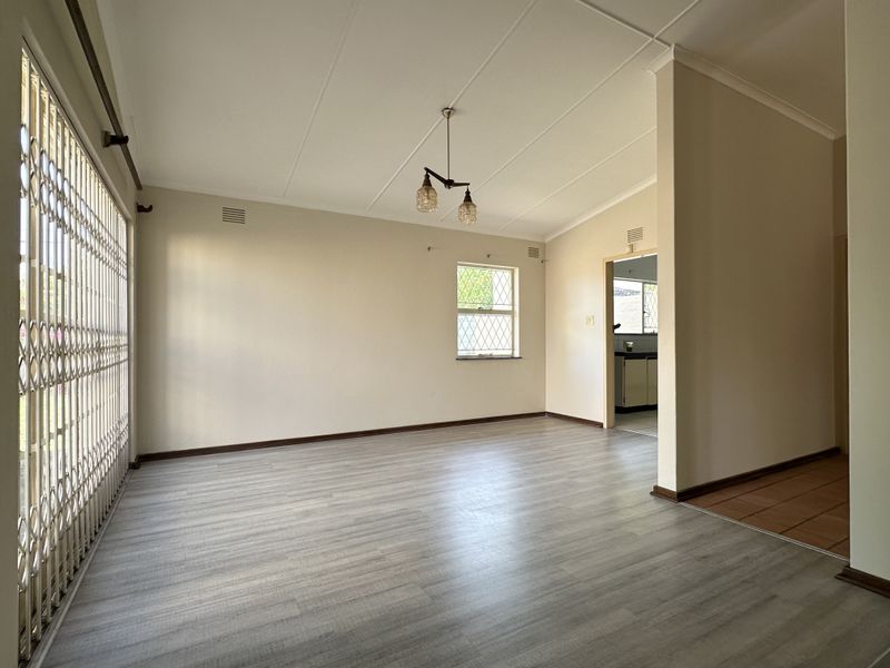 A bright, empty living room featuring modern laminate flooring, a security gate, and neutral wall finishes, offering a clean canvas for personalization.
