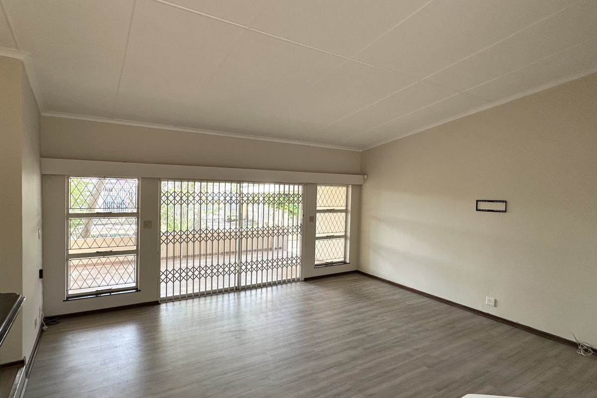 Spacious, light-filled living room featuring modern laminate flooring, large windows, and sliding glass doors with security gates leading to the outdoor area.
