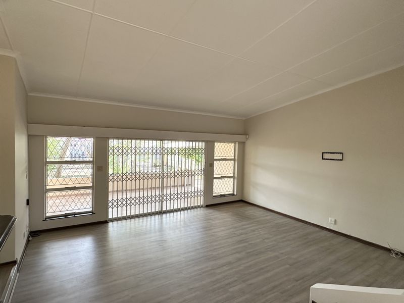 Spacious, light-filled living room featuring modern laminate flooring, large windows, and sliding glass doors with security gates leading to the outdoor area.