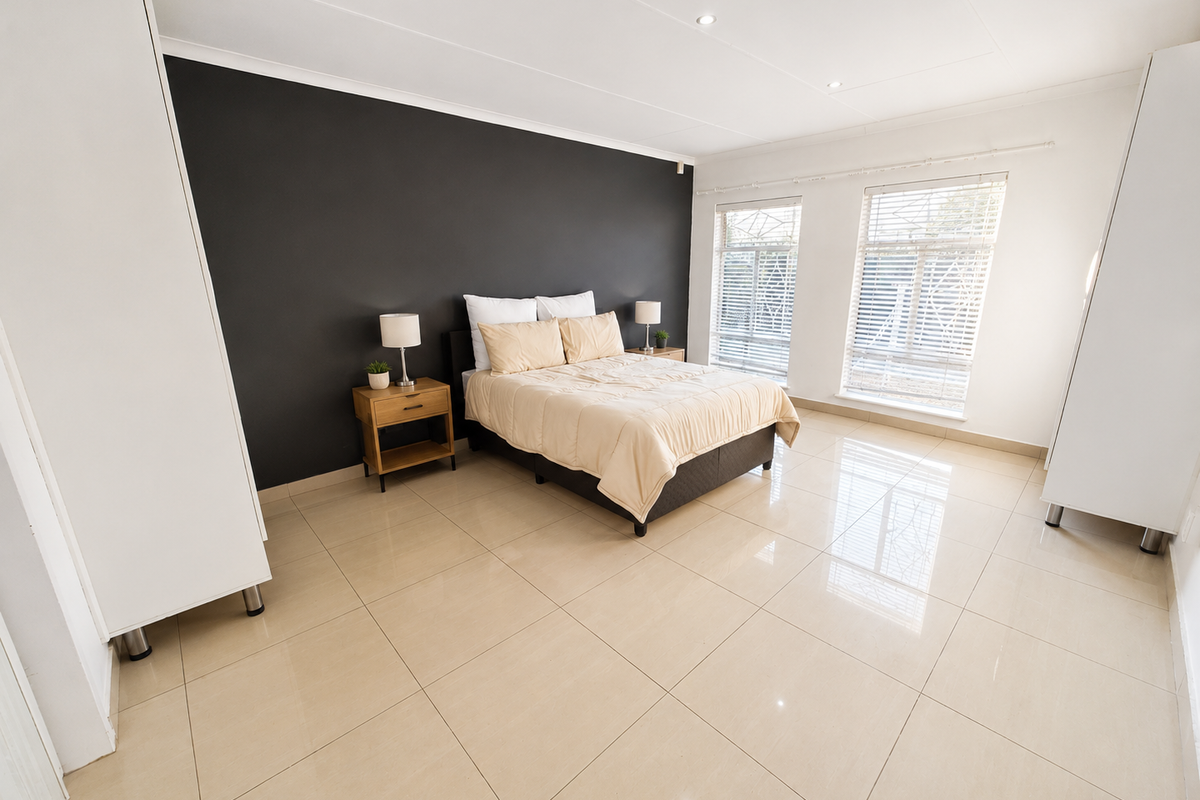Spacious bedroom featuring large format floor tiles, built-in cupboards, a dark feature wall, and dual windows with venetian blinds.