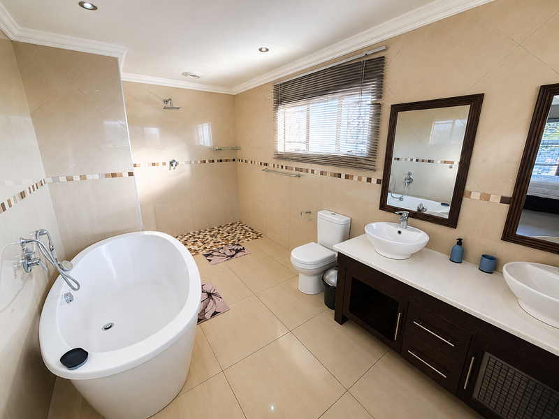 Modern bathroom featuring a freestanding bathtub, walk-in shower, and a double vanity with vessel sinks, finished with neutral wall and floor tiles.
