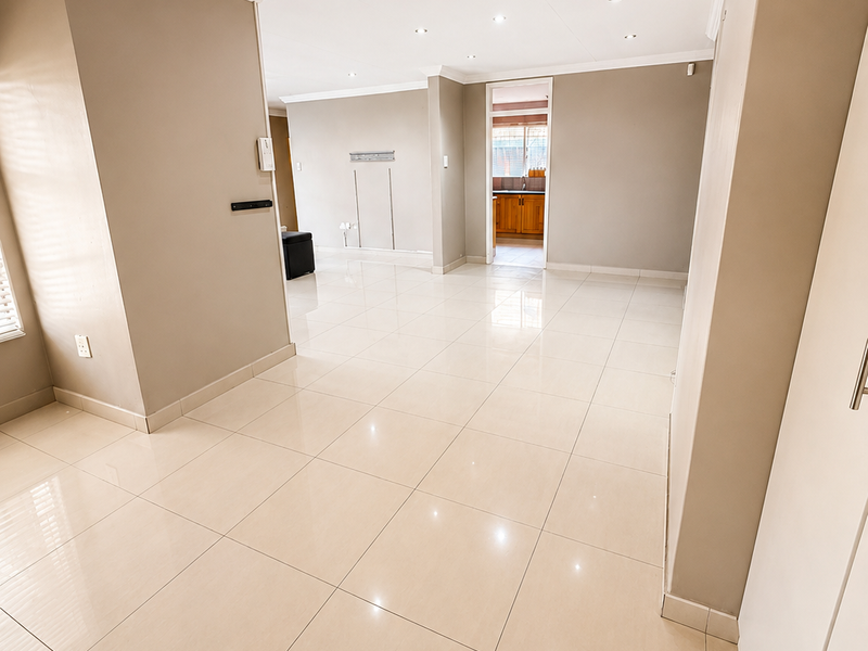 Spacious open-plan living area featuring neutral walls, polished porcelain floor tiles, recessed lighting, and crown molding, leading through to a kitchen area.