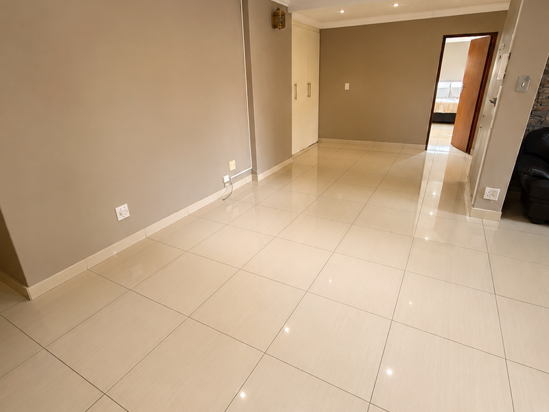 A bright, empty living area featuring neutral walls, polished tiled flooring, recessed downlighting, and crown molding, with a built-in cupboard for storage.