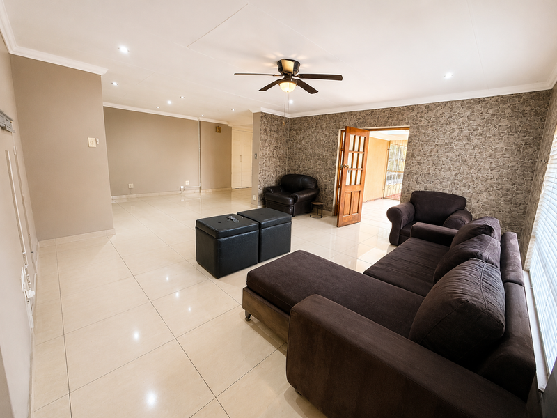 Spacious living room featuring large format floor tiles, recessed lighting, a ceiling fan, and a feature wall with textured wallpaper.