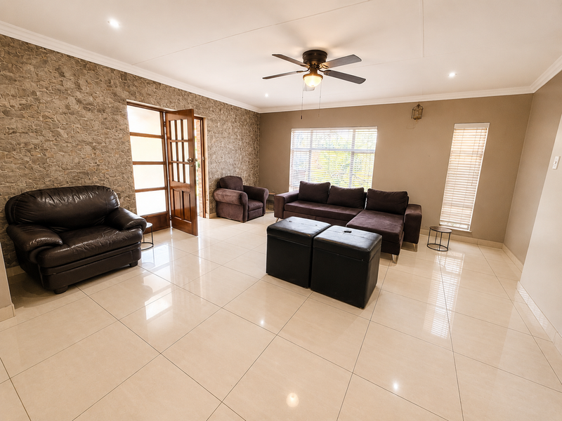 Spacious living room featuring large format floor tiles, a textured stone feature wall, ceiling fan, and natural light through timber-framed doors and windows.