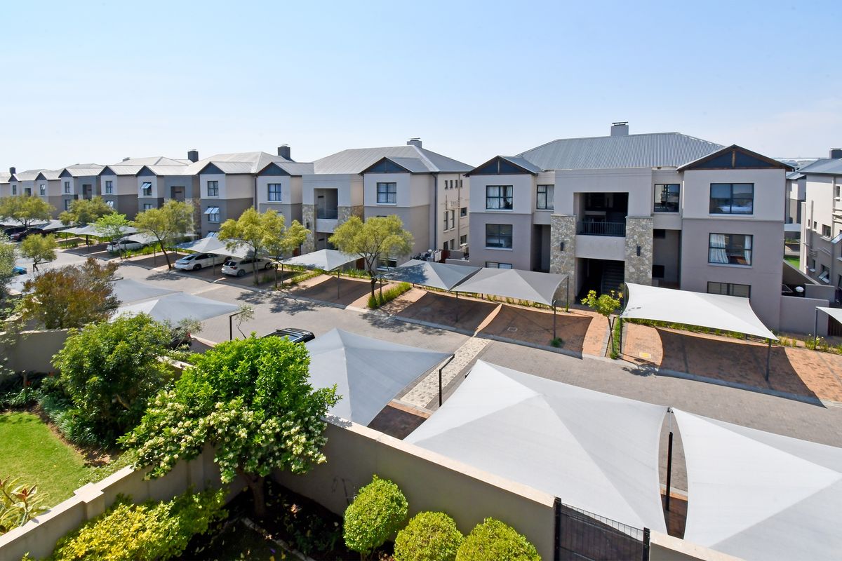 Aerial view of a modern apartment complex featuring paved driveways, shade cloth carports, and well-maintained landscaped garden areas.