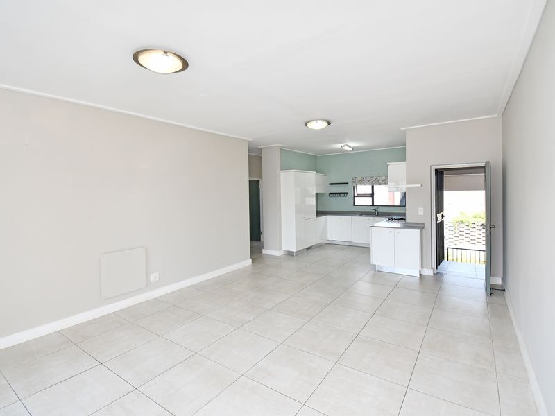 Spacious open-plan living area featuring neutral tiled flooring, modern kitchen cabinetry with integrated appliances, and direct access to an outdoor balcony area.