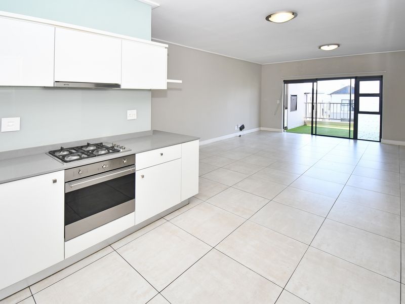 Spacious open-plan kitchen and living area featuring modern cabinetry, built-in appliances, tiled flooring, and direct access to a balcony through sliding glass doors.
