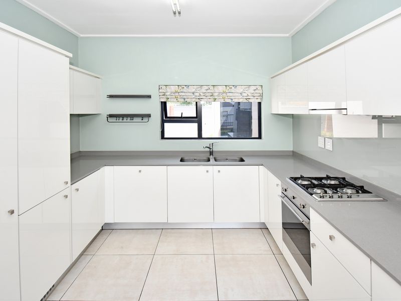 Modern kitchen featuring white high-gloss cabinetry, stone countertops, integrated gas hob, oven, and extractor fan with neutral tiled flooring.