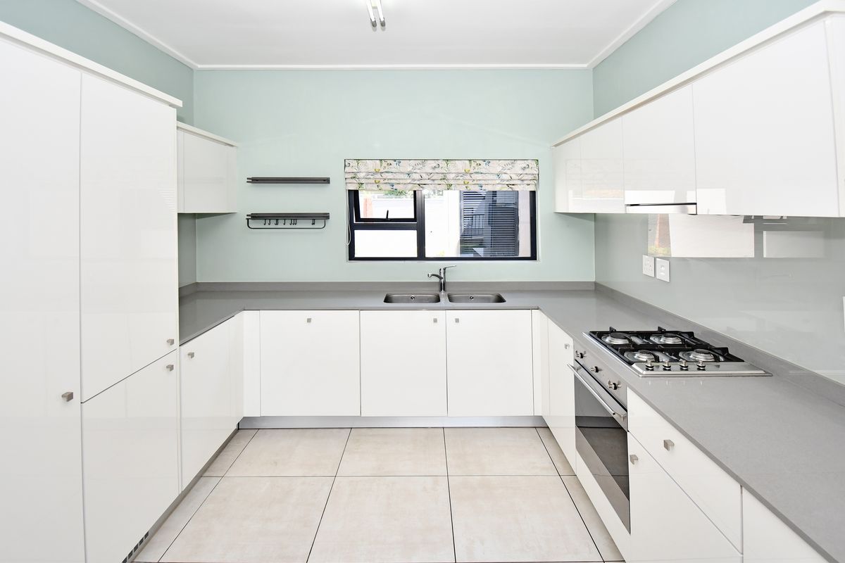 Modern kitchen featuring white high-gloss cabinetry, stone countertops, integrated gas hob, oven, and extractor fan with neutral tiled flooring.