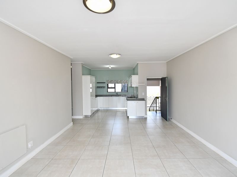 An open-plan living and kitchen area featuring neutral tiled flooring, modern cabinetry, and a functional layout with direct access to an exterior entrance.