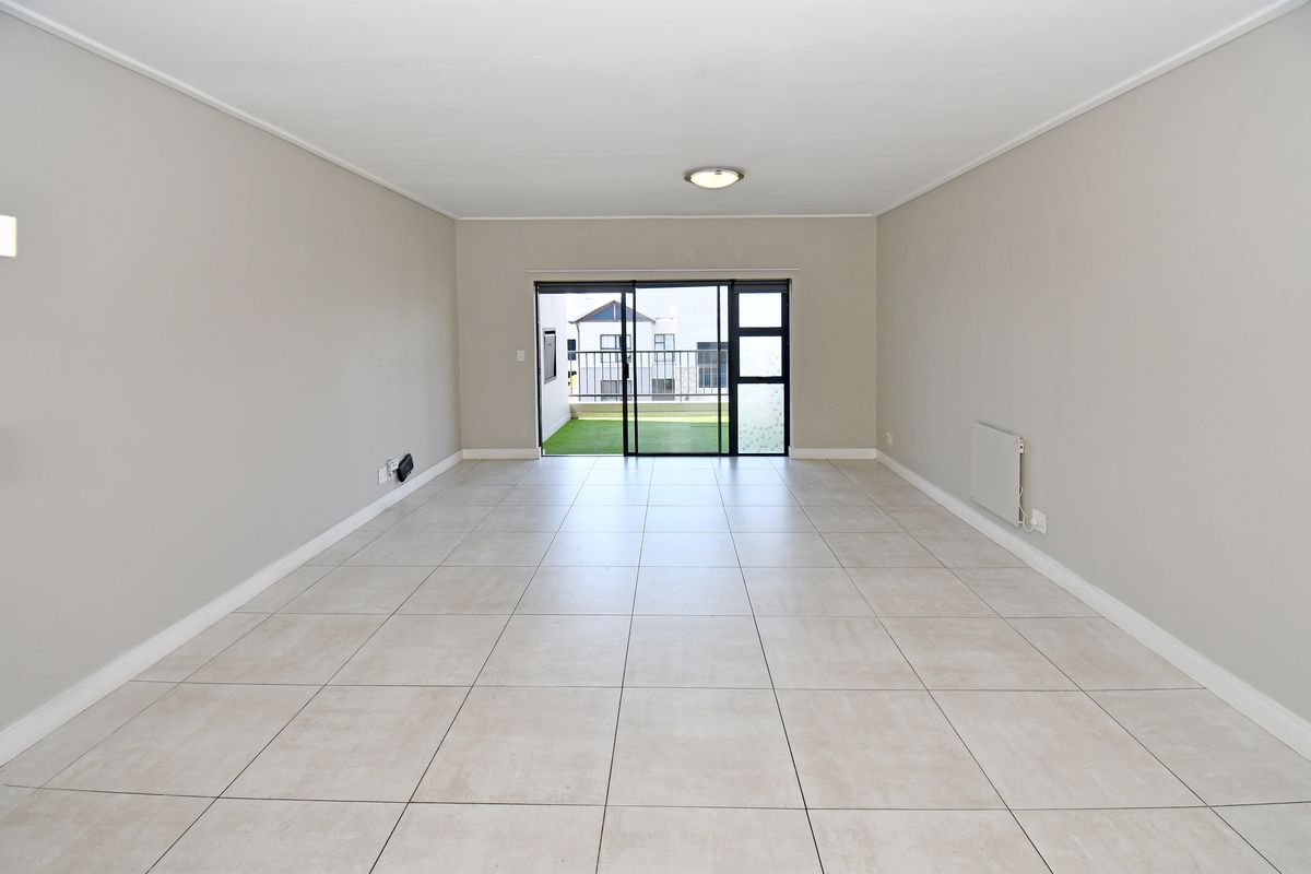A spacious, empty living area featuring neutral tiled flooring, a wall-mounted heater, and large sliding glass doors leading to an outdoor balcony.