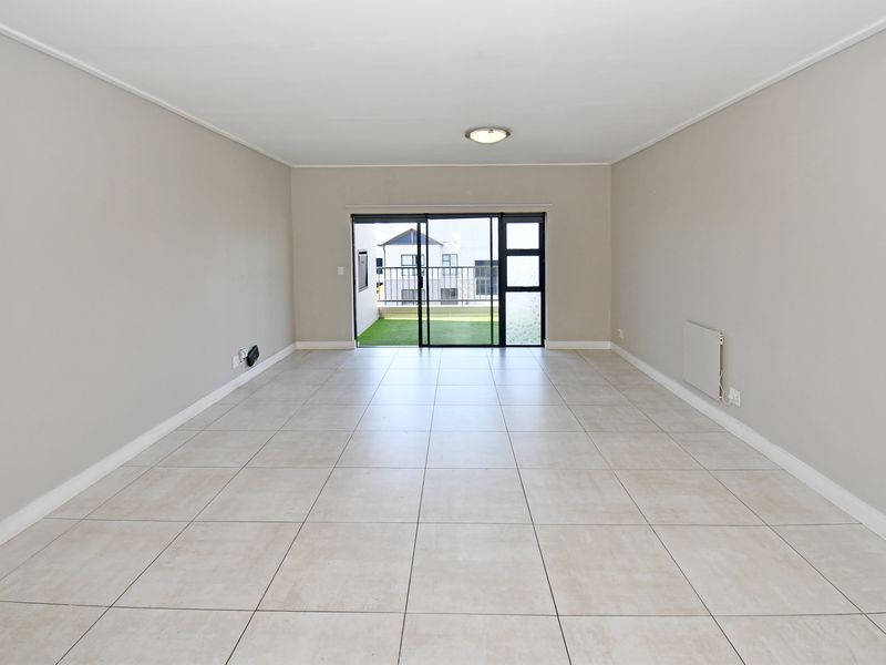 A spacious, empty living area featuring neutral tiled flooring, a wall-mounted heater, and large sliding glass doors leading to an outdoor balcony.