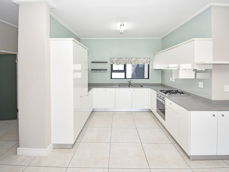 Modern kitchen featuring white high-gloss cabinetry, stone countertops, integrated gas hob, oven, and extractor fan with neutral tiled flooring.