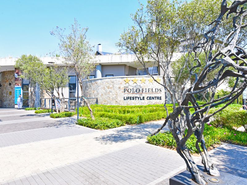 Exterior view of The Polo Fields Lifestyle Centre featuring stone-clad walls, manicured gardens, and paved walkways.