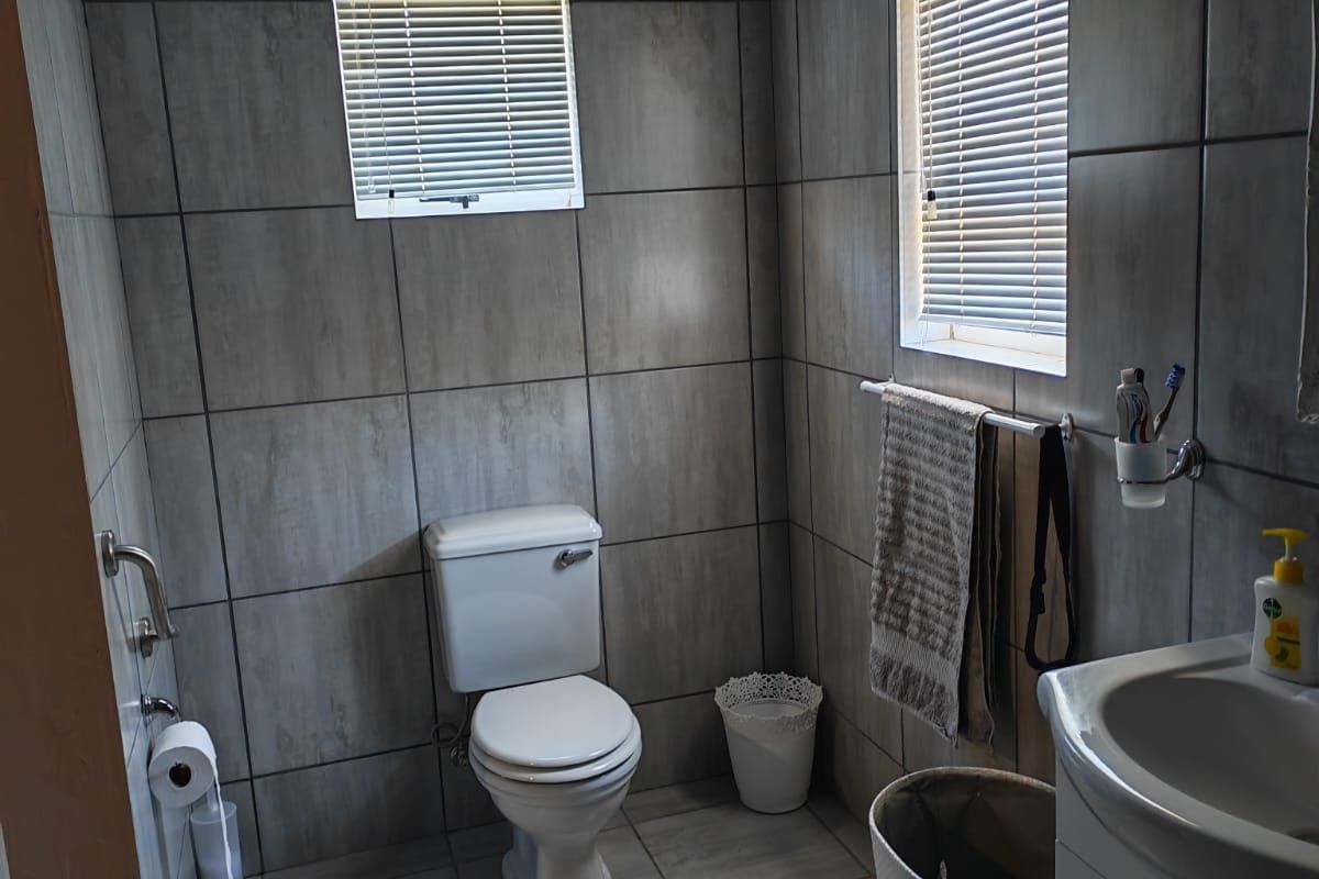 A modern bathroom featuring floor-to-ceiling grey tiling, a white ceramic toilet, and a vanity basin with built-in storage.