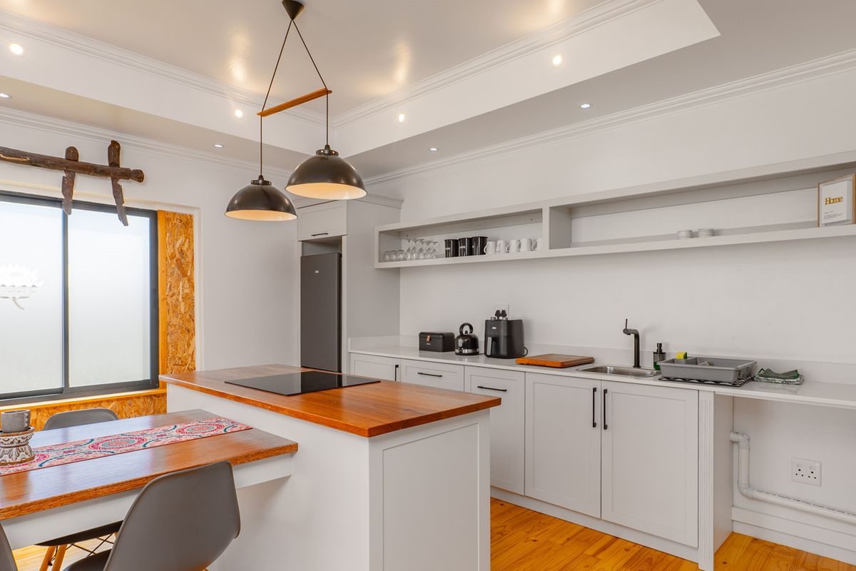 Modern kitchen featuring a central island with a wooden countertop, induction hob, sleek cabinetry, open shelving, and warm timber flooring.