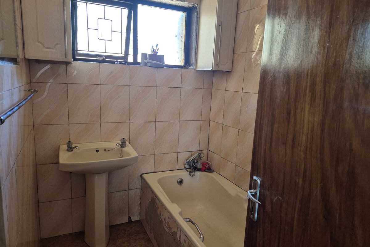 A compact bathroom featuring a pedestal basin, a bathtub with integrated fixtures, and wall-to-wall tiling, requiring some cosmetic updates.