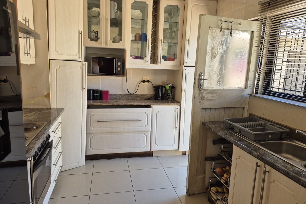 A functional kitchen featuring light-toned cabinetry, granite-look countertops, a built-in oven, and a stainless steel sink with tiled flooring.