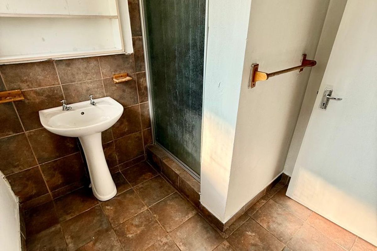 A compact bathroom featuring a pedestal basin, shower enclosure, and tiled finishes, presenting an opportunity for modernization and aesthetic updates.