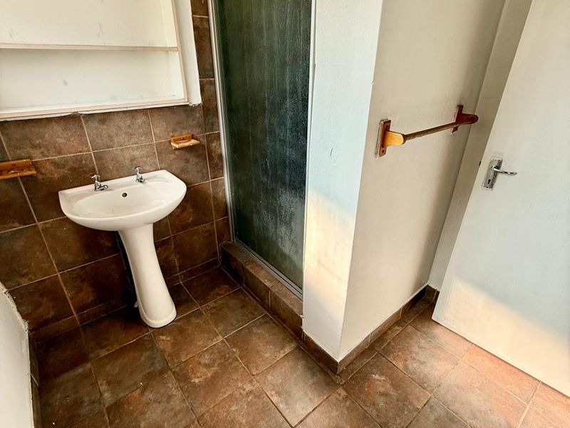 A compact bathroom featuring a pedestal basin, shower enclosure, and tiled finishes, presenting an opportunity for modernization and aesthetic updates.