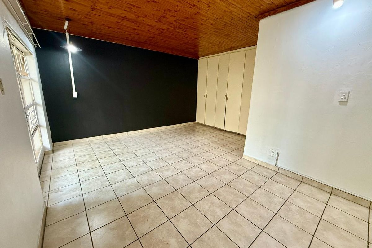 An empty bedroom featuring tiled flooring, built-in cupboards, and a timber-paneled ceiling, offering a blank canvas for personalization.