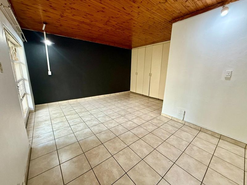An empty bedroom featuring tiled flooring, built-in cupboards, and a timber-paneled ceiling, offering a blank canvas for personalization.