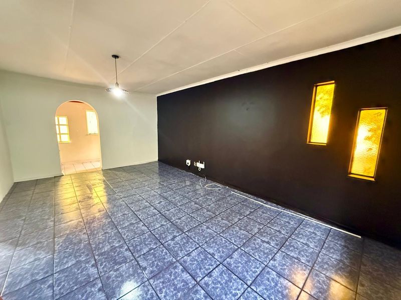 An empty living room featuring tiled flooring, a distinctive arched doorway, and decorative recessed wall lighting.