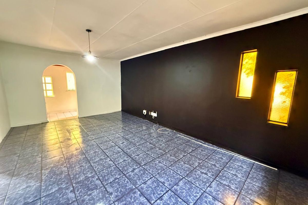 An empty living room featuring tiled flooring, a distinctive arched doorway, and decorative recessed wall lighting.