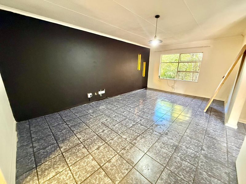 An empty living room featuring dark accent wall, tiled flooring, and natural light from a large window.