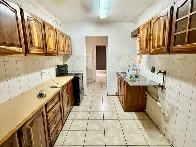 A galley-style kitchen featuring wooden cabinetry, tiled flooring, and a freestanding stove, offering a functional layout in need of cosmetic updates.