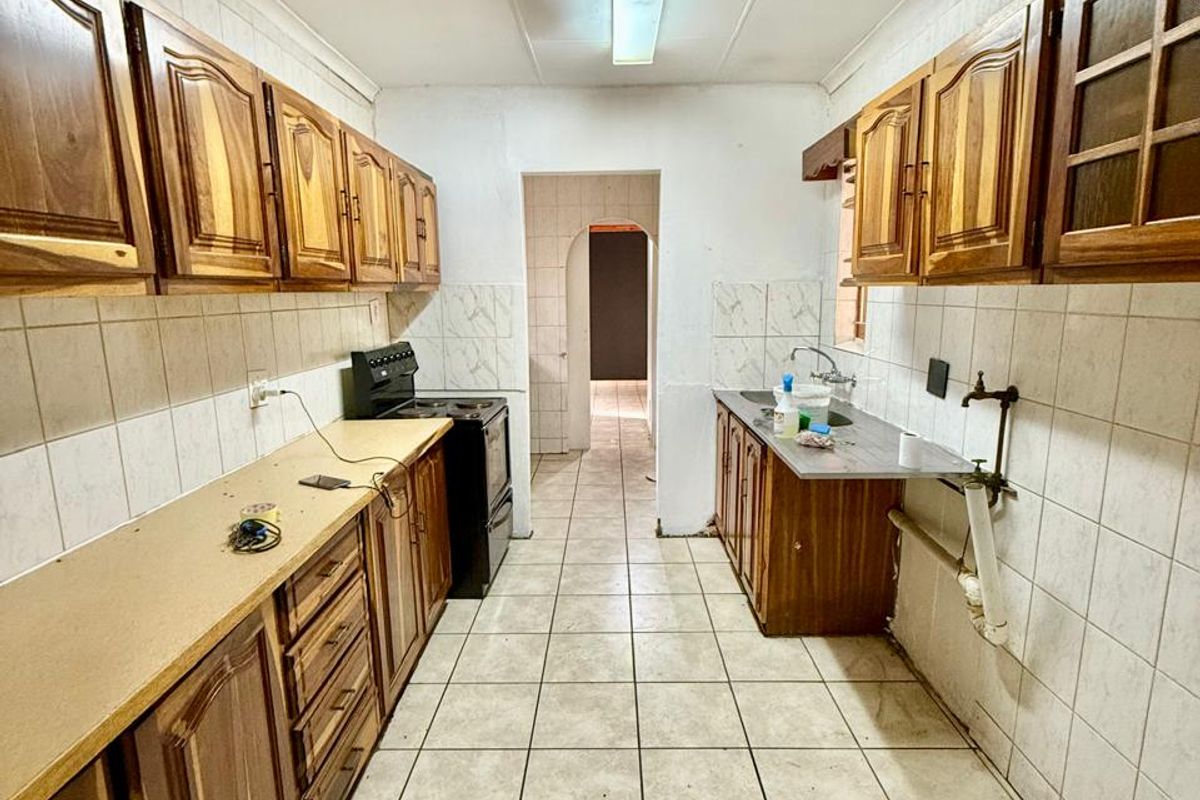 A galley-style kitchen featuring wooden cabinetry, tiled flooring, and a freestanding stove, offering a functional layout in need of cosmetic updates.