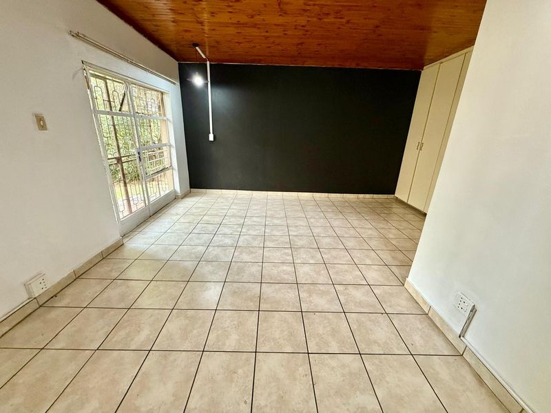 An empty bedroom featuring tiled flooring, a wooden ceiling, built-in cupboards, and a security gate leading to the exterior.