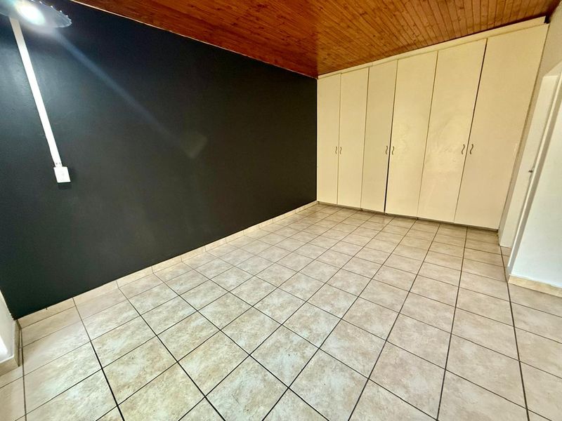 An empty bedroom featuring tiled flooring, built-in cupboards, and a timber-paneled ceiling.