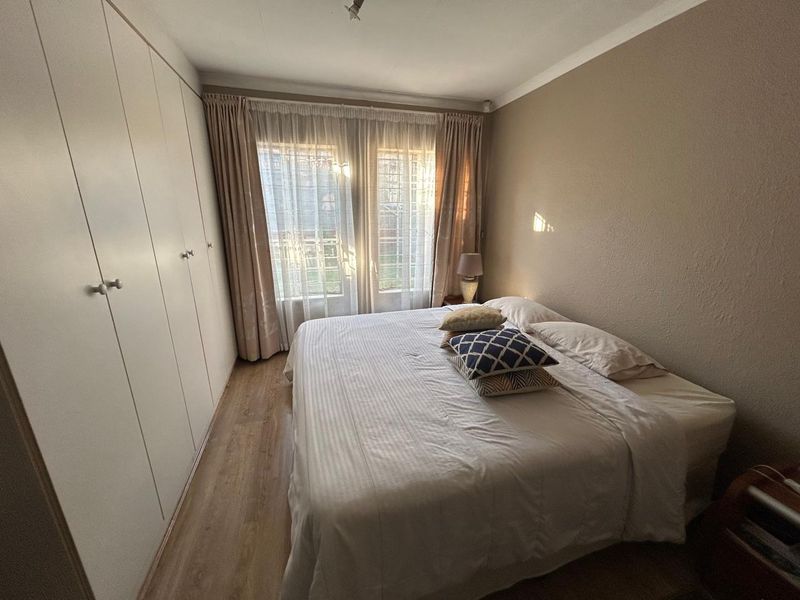 A functional bedroom featuring laminate flooring, built-in cupboards for storage, and large windows fitted with security bars.