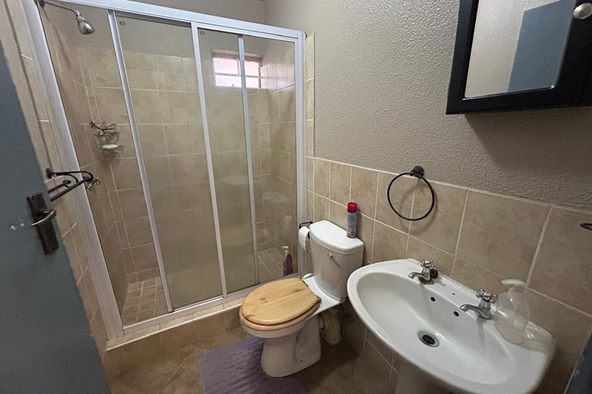 A functional bathroom featuring a shower enclosure, pedestal basin, and toilet with neutral wall and floor tiling.