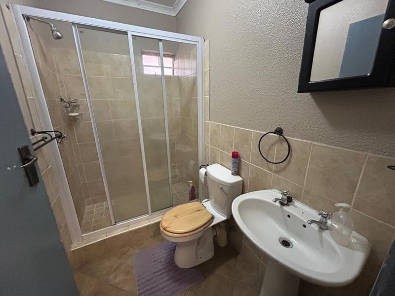 A functional bathroom featuring a shower enclosure, pedestal basin, and toilet with neutral wall and floor tiling.