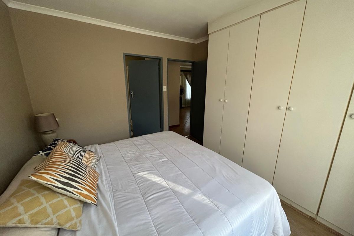 A bedroom featuring built-in cupboards, laminate flooring, and neutral wall tones, providing a functional and well-lit sleeping space.