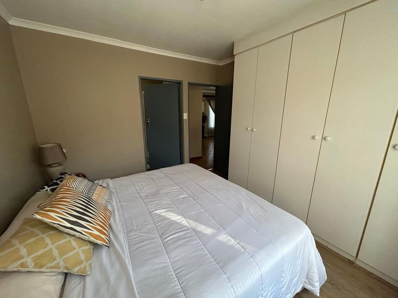 A bedroom featuring built-in cupboards, laminate flooring, and neutral wall tones, providing a functional and well-lit sleeping space.