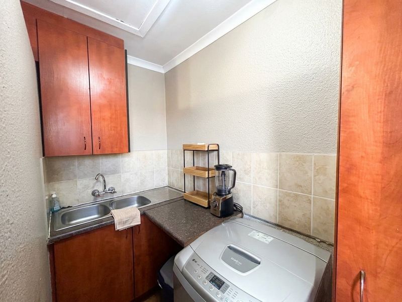 A functional laundry area featuring built-in cabinetry, a double bowl stainless steel sink, and tiled splashback, providing practical utility space.