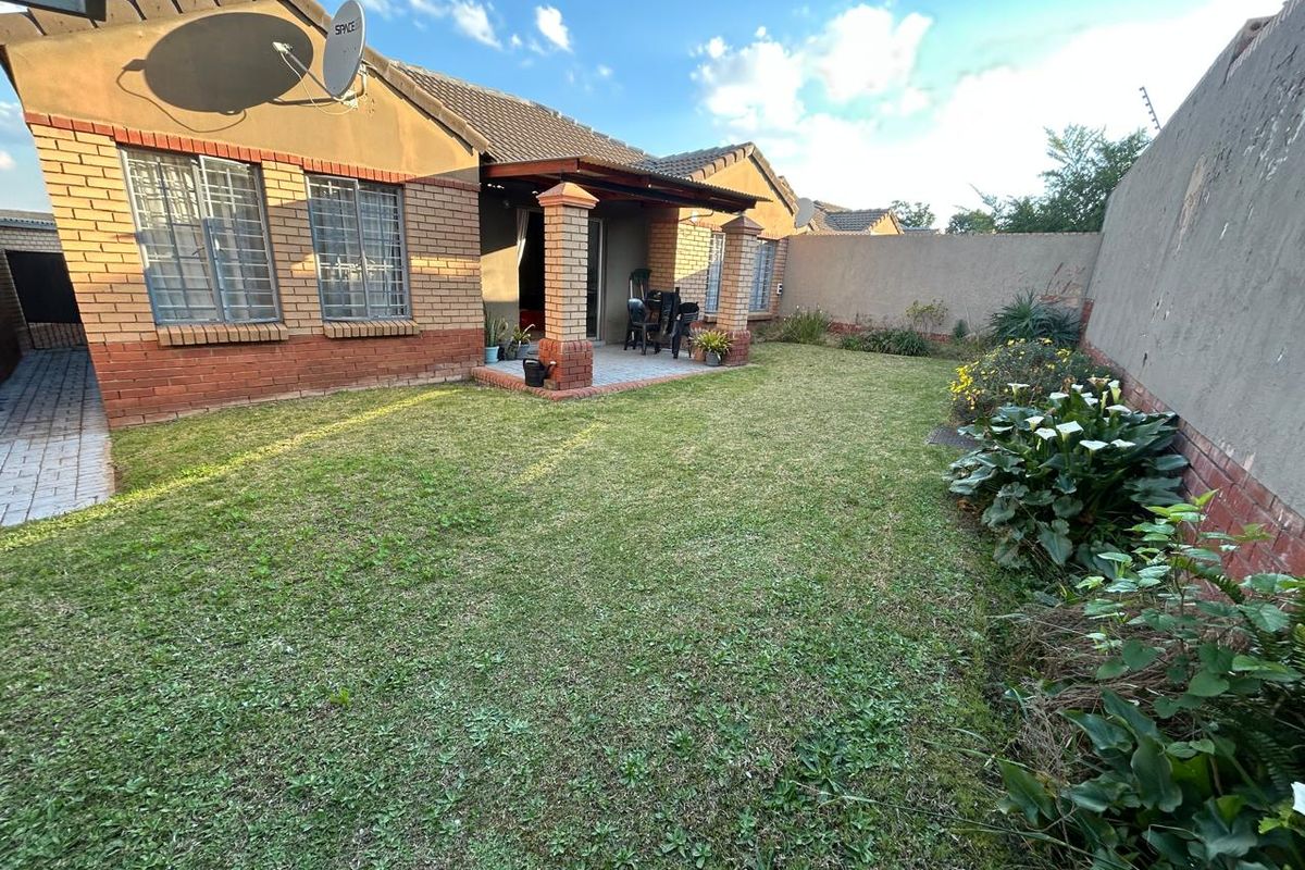 Rear view of the townhouse featuring a private garden, a covered patio area with brick pillars, and secure window bars.