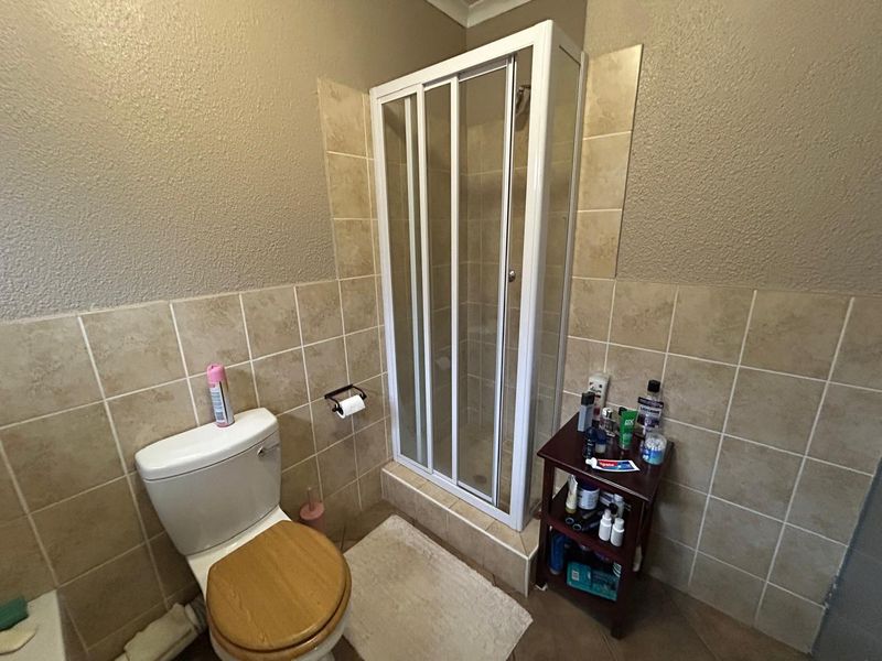 A functional bathroom featuring a corner shower enclosure, a standard toilet, and neutral wall tiling.