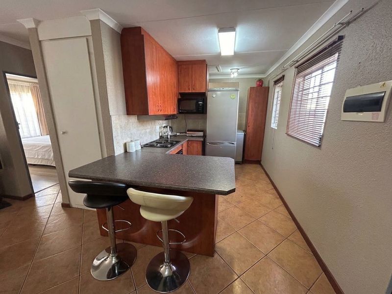 A functional kitchen featuring wood-finish cabinetry, laminate countertops, a built-in hob, and tiled flooring, with an integrated breakfast bar area.