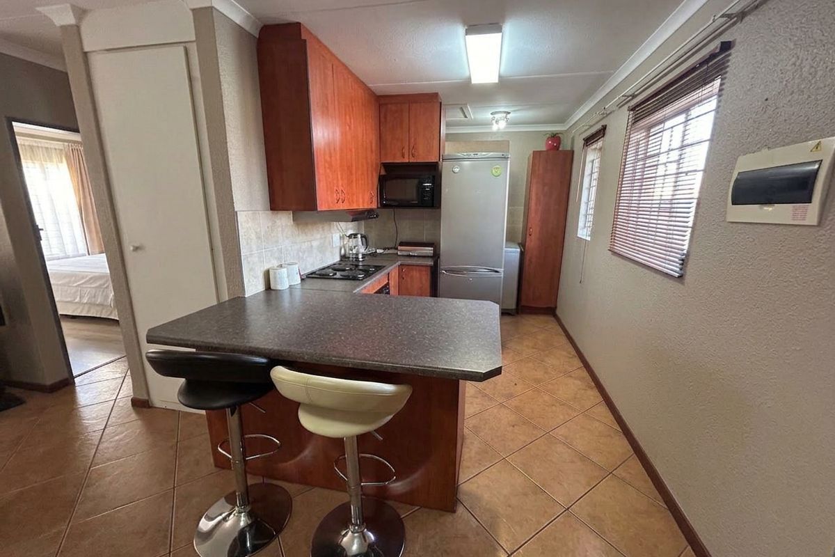 A functional kitchen featuring wood-finish cabinetry, laminate countertops, a built-in hob, and tiled flooring, with an integrated breakfast bar area.