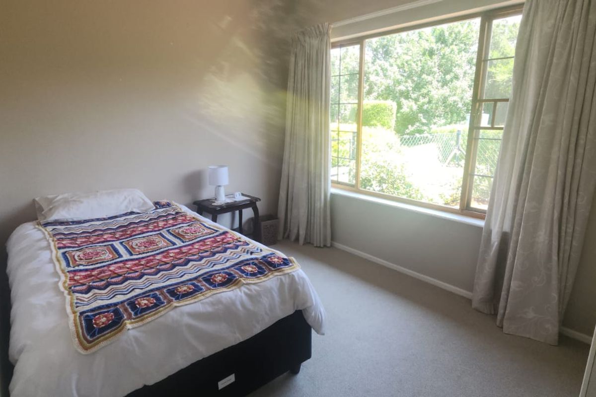 A bedroom featuring neutral carpeting, built-in wardrobe storage, and a large window providing natural light and garden views.
