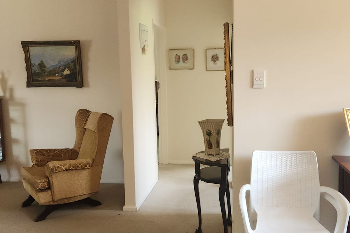 A view of a living area featuring neutral wall finishes and carpeted flooring, leading into a central hallway.
