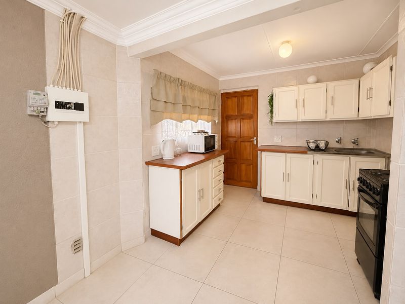 Functional kitchen featuring white cabinetry, laminate countertops, tiled finishes, and a freestanding stove, with visible electrical distribution board and conduit.