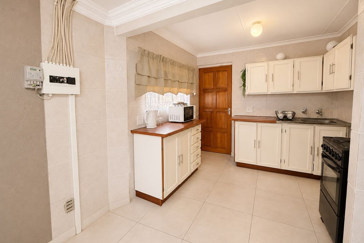 Functional kitchen featuring white cabinetry, laminate countertops, tiled finishes, and a freestanding stove, with visible electrical distribution board and conduit.