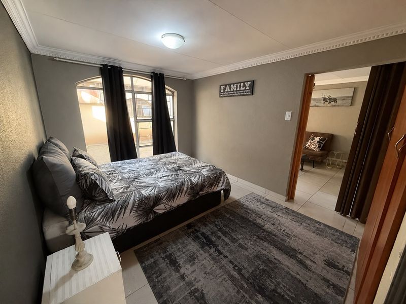 A well-lit bedroom featuring tiled flooring, decorative ceiling cornicing, and an arched window, providing a comfortable and functional living space.